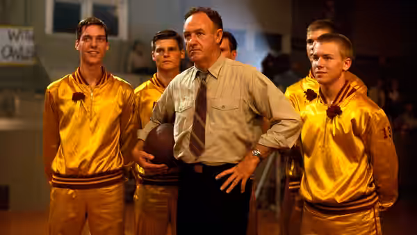 Norman Dale (Gene Hackman) stands with a basketball among players in gold warmups
