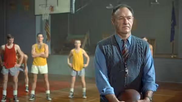 Norman Dale (Gene Hackman) holds a basketball while players wait on the gym court