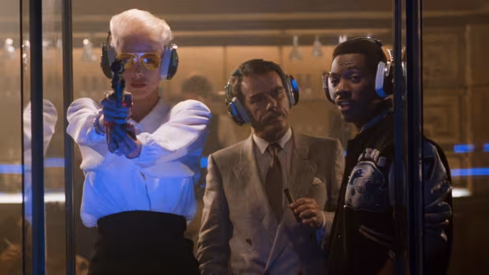 Karla Fry (Brigitte Nielsen) aims a gun beside Maxwell Dent and Axel Foley behind glass