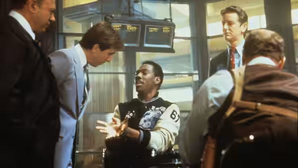 Axel Foley gestures to police officers gathered around him in a station