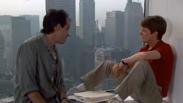 Brantley Foster sits by a skyscraper window talking with a colleague