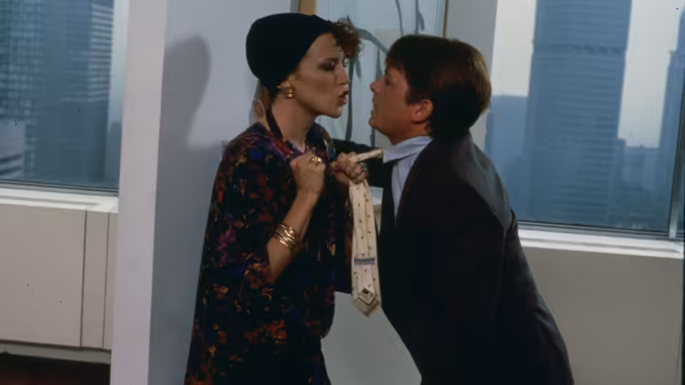 Brantley Foster (Michael J. Fox) leans toward Vera Prescott as she grips his tie in an office