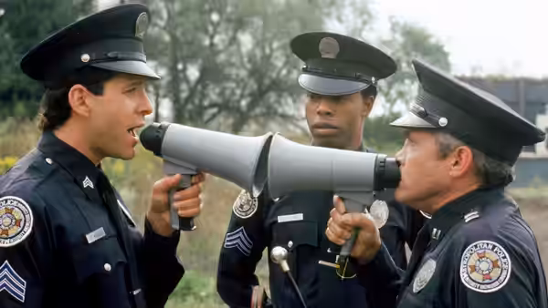 Three uniformed officers gather around a megaphone as one speaks into its mouthpiece