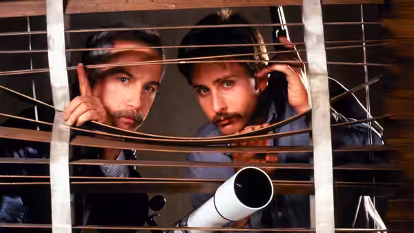 Chris Lecce (Richard Dreyfuss) and Bill Reimers (Emilio Estevez) peer through blinds beside a telescope