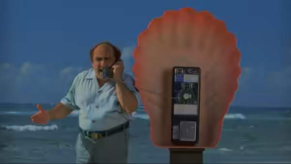 Owen Lift (Danny DeVito) talks on a shell-shaped payphone beside the ocean