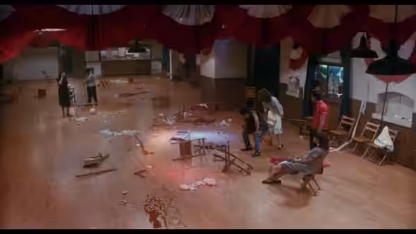 People survey a wrecked hall scattered with chairs, debris and water