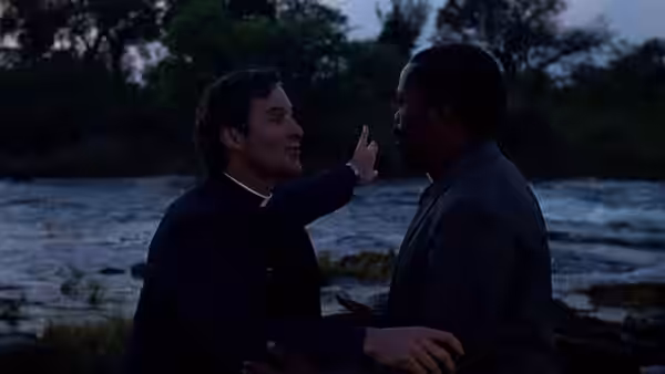 Donald Woods (Kevin Kline), dressed as a priest, speaks with a man beside a river