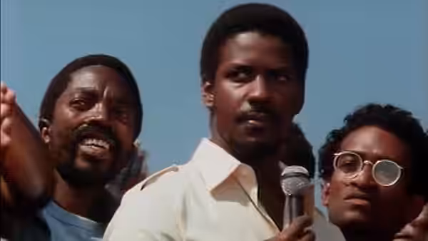 Steve Biko (Denzel Washington) holds a microphone among men at an outdoor rally
