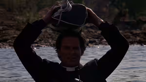 Donald Woods (Kevin Kline), dressed as a priest, lifts a bag above his head in the river