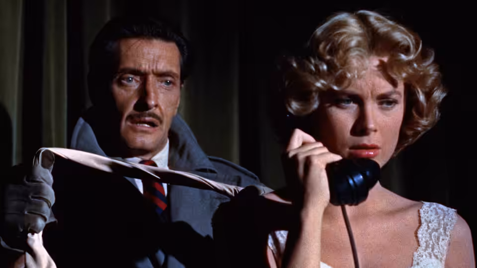 Tony Wendice (Ray Milland) stands behind Margot Wendice (Grace Kelly) holding a tie as she speaks on the phone
