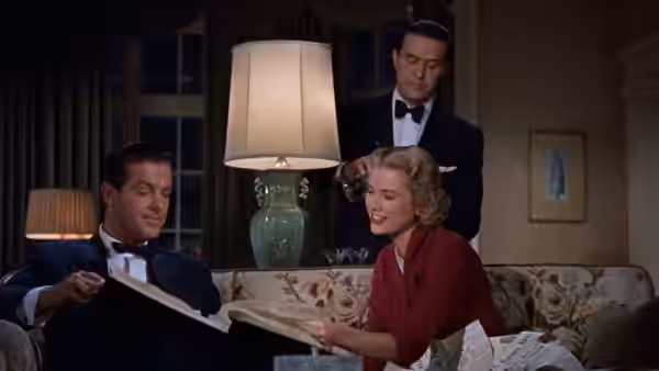 Tony Wendice (Ray Milland) and Margot Wendice (Grace Kelly) examine papers with a man standing behind them