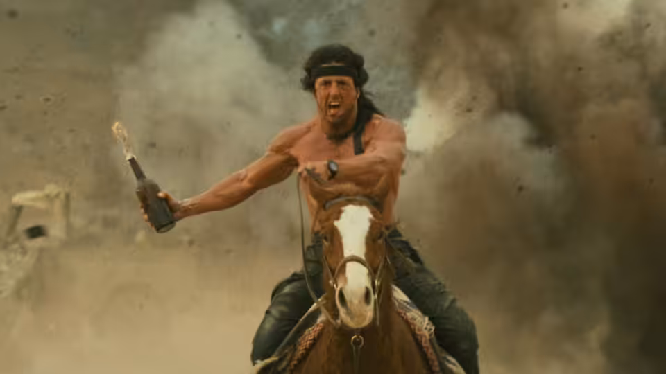 John Rambo (Sylvester Stallone) rides a horse through smoke, gripping a pistol