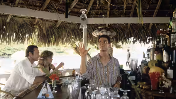 Brian Flanagan juggles a bottle behind a tiki bar as Doug Coughlin and a woman sit nearby