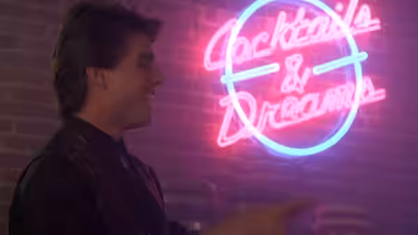 Brian Flanagan stands beside a glowing Cocktails & Dreams neon sign