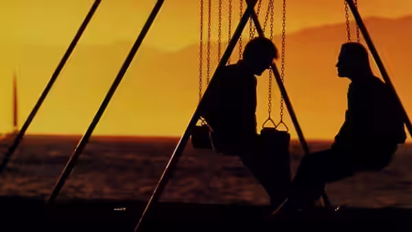 Two silhouetted figures sit facing each other on a boat at sunset