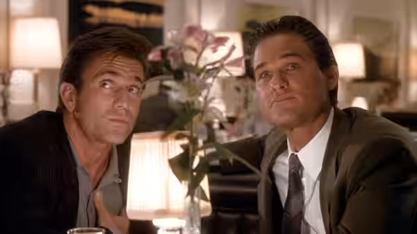 Dale McKussic (Mel Gibson) and Nick Frescia (Kurt Russell) look upward from a table