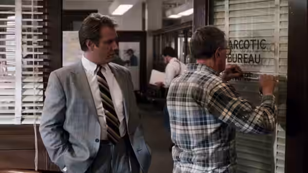 Lieutenant Nick Frescia (Kurt Russell) watches a man write on a glass office partition