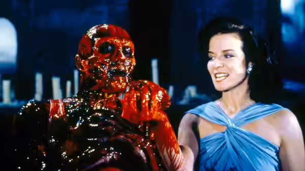 Julia Cotton (Clare Higgins) stands beside bloodied Frank Cotton (Sean Chapman) in a dim room