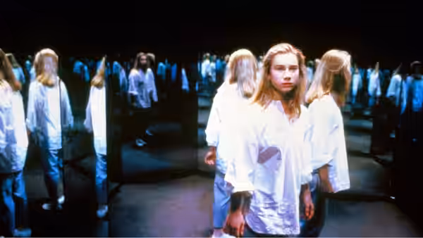 Tiffany stands among rows of white-clad girls in a dark mirrored chamber