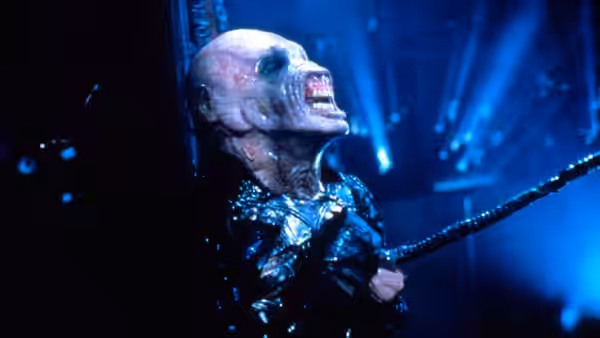 The Channard Cenobite screams as a tentacle extends from his body in a blue-lit chamber