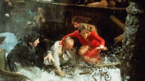 A woman in red and two men struggle through a flooded room