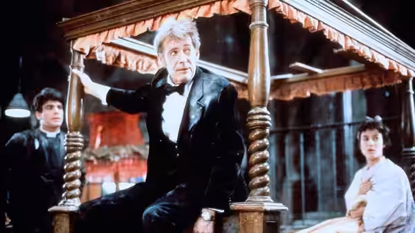 Peter Plunkett (Peter O'Toole) sits on a carved bed as two people watch