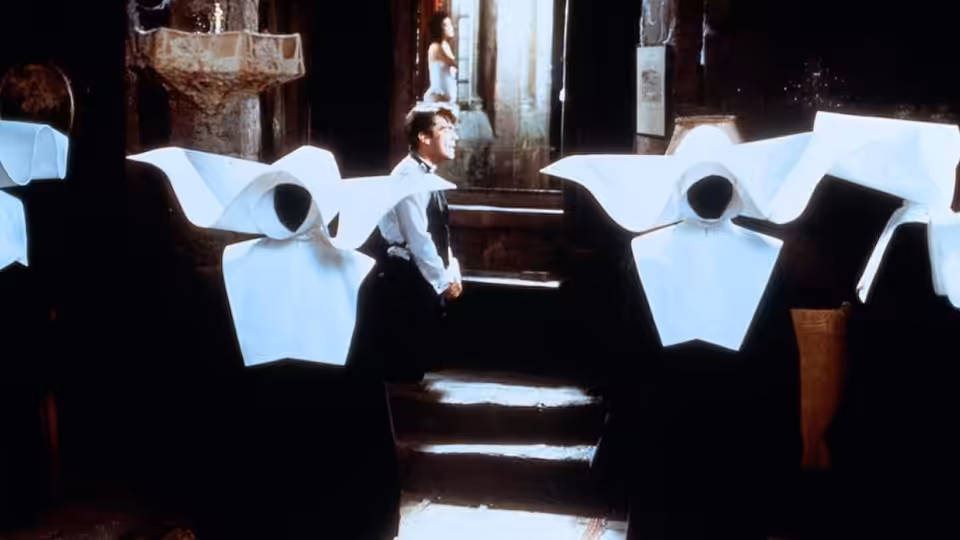A man stands on a staircase amid oversized paper cutouts in a dim room