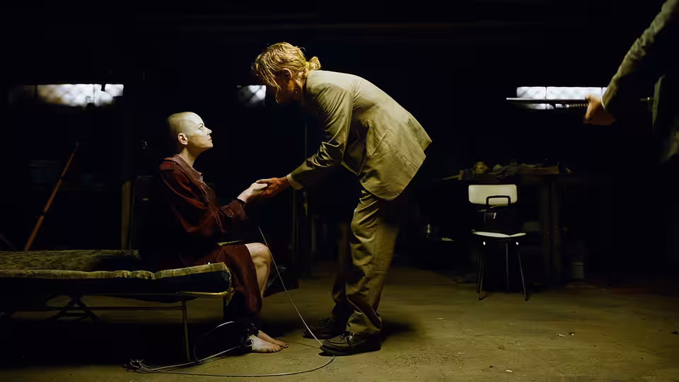 Bald Michelle (Emma Stone) on a cot looks up at a suited man leaning over her