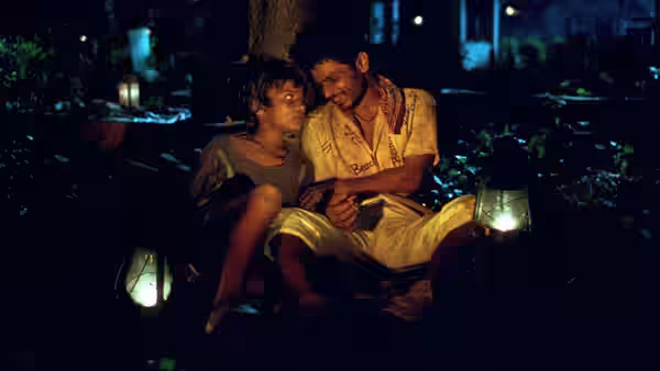 Two boys sit close together at night beside a glowing lantern