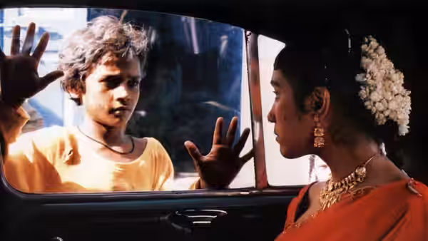 A boy presses his hands against a car window as a girl watches