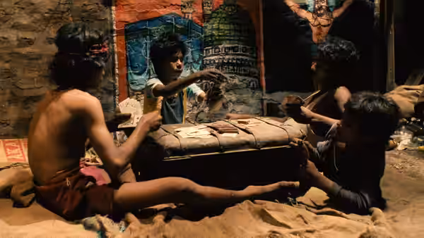 Boys sit around a low table playing cards in a cramped room
