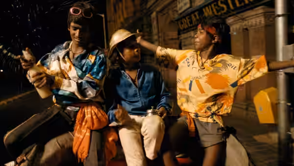 Three boys sit together on a nighttime street, one wearing a helmet