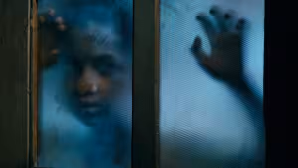 A face and raised hand appear behind a fogged glass panel