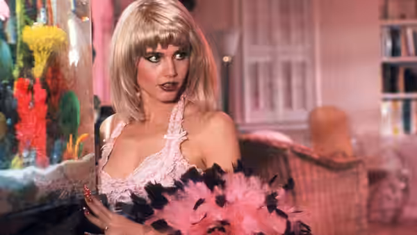 Candy Pink (Julie Brown) holds a feather boa beside a colorful aquarium