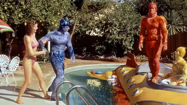 Valerie (Geena Davis) approaches Mac beside a swimming pool as Wiploc stands on a diving board