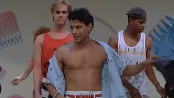 Three young men dance together, one wearing an open shirt and striped shorts