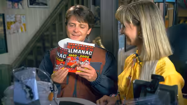 Marty McFly (Michael J. Fox) studies a sports almanac while Lorraine (Lea Thompson) looks on