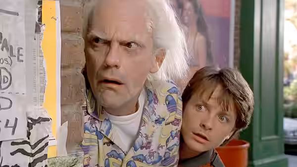 Doc Brown (Christopher Lloyd) and Marty McFly (Michael J. Fox) peek around a wall covered with notices