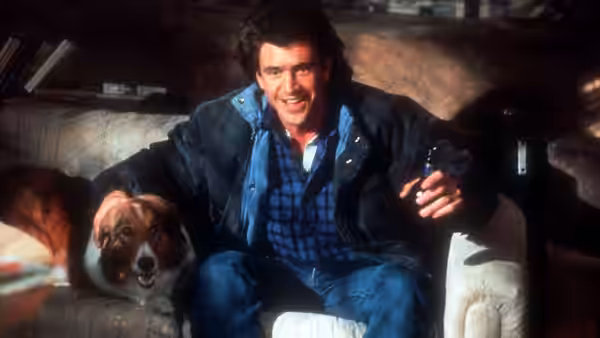 Martin Riggs (Mel Gibson) sits on a couch beside a dog