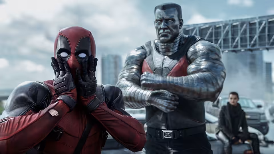 Deadpool (Ryan Reynolds) covers his face beside Colossus with crossed arms