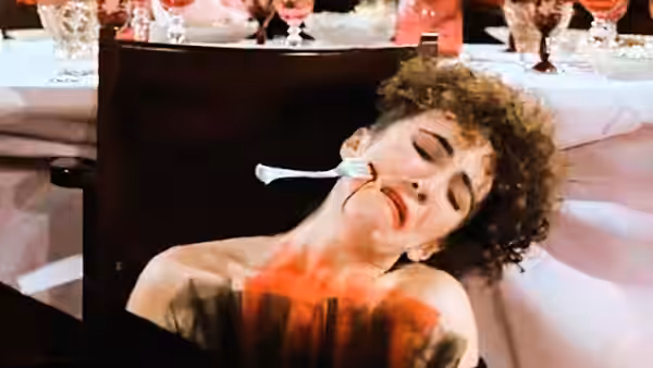 Georgina Spica (Helen Mirren) reclines beside a dining table with a spoon at her lips