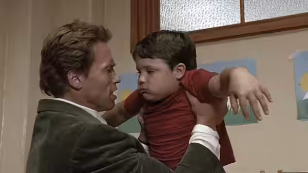 Kimble (Arnold Schwarzenegger) lifts a frowning boy in a school hallway