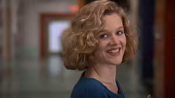 Joyce (Penelope Ann Miller) smiles over her shoulder in a school hallway