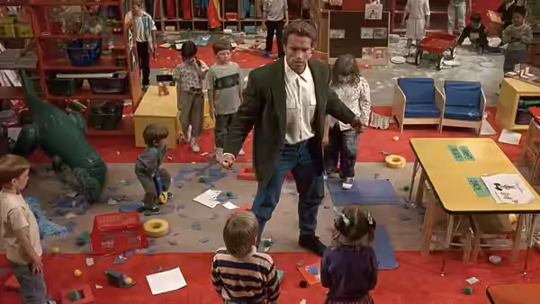 Kimble (Arnold Schwarzenegger) stands among children in a cluttered kindergarten classroom