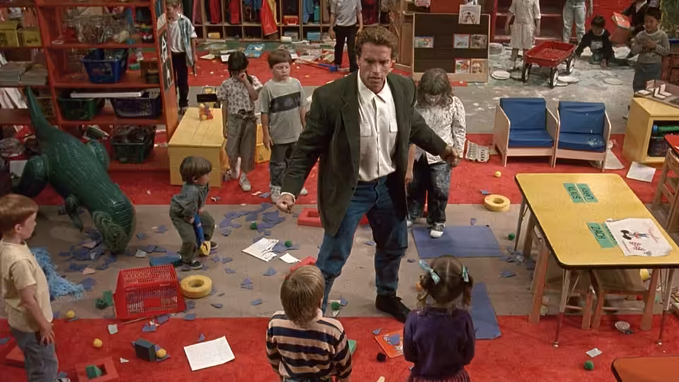 Kimble (Arnold Schwarzenegger) stands among children in a cluttered kindergarten classroom
