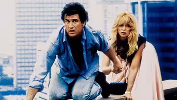 Rick Jarmin (Mel Gibson) crouches beside Marianne Graves (Goldie Hawn) on a city rooftop