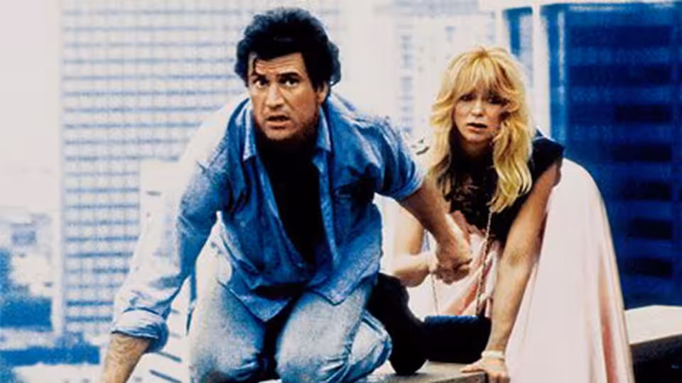 Rick Jarmin (Mel Gibson) crouches beside Marianne Graves (Goldie Hawn) on a city rooftop