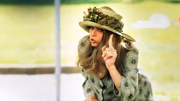 Mollie (Kirstie Alley) wears a decorated hat and raises one finger