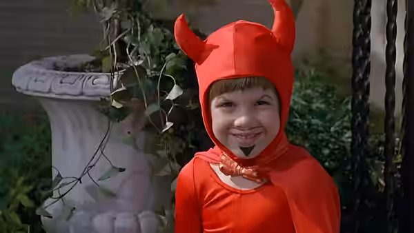 Junior (Michael J. Oliver) smiles in a red devil costume beside a garden fountain