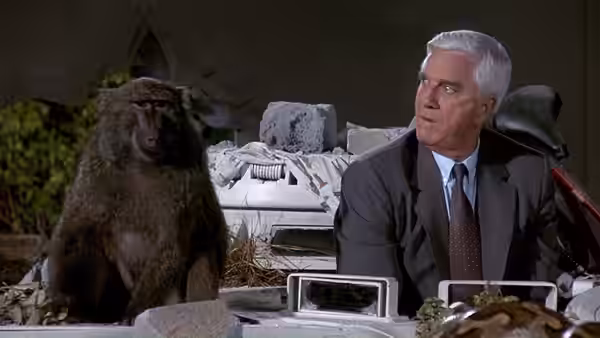 Frank Drebin (Leslie Nielsen) sits beside a baboon among laboratory equipment